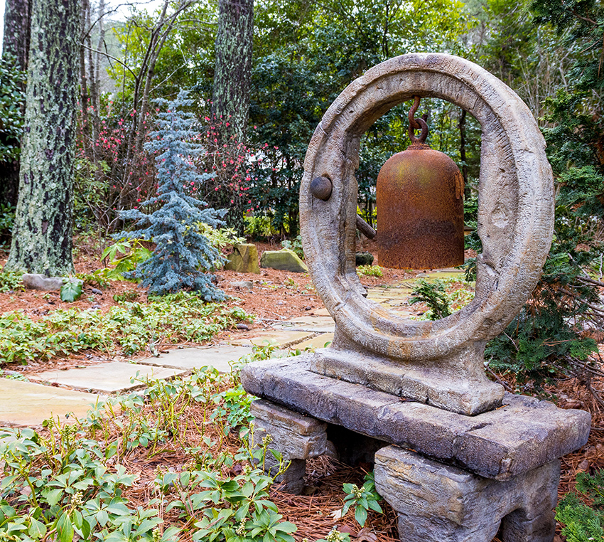 A cast iron bell hangs in garden landscape