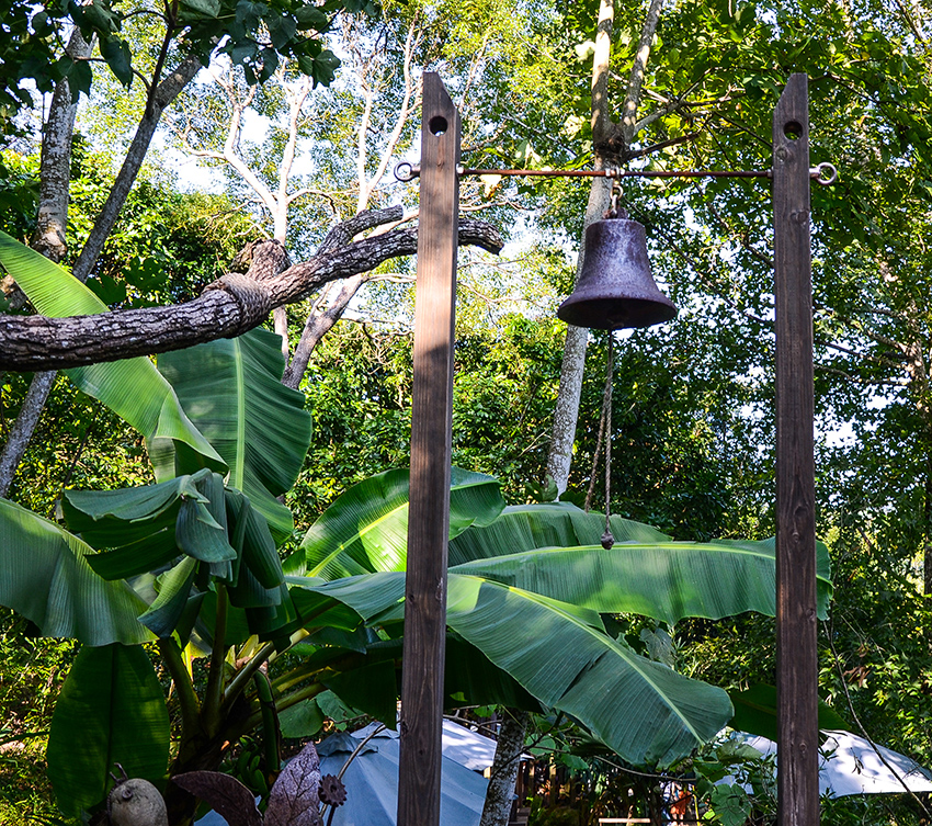 Bell hangs from a stand in a tropical garden