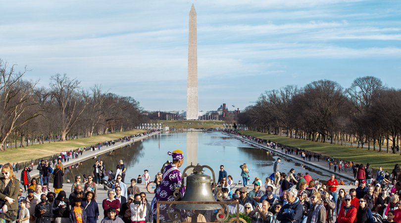Trinette Chase rings a bell before a large crowd with the Washington Monument in the distance