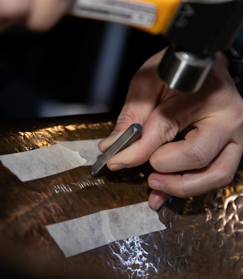 A sailor engraves the name of his son on the lip of a ship's bell after baptism