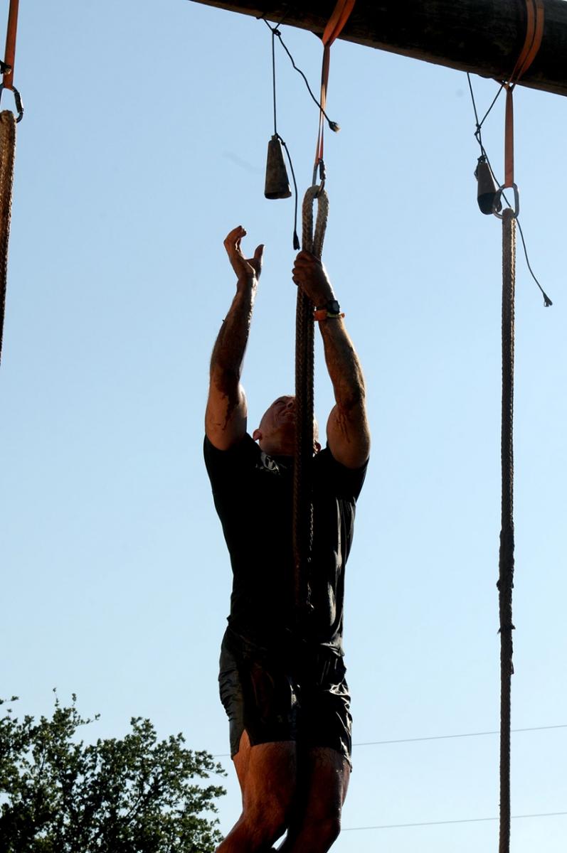 Spartan Race competitor climbs a rope and rings a bell