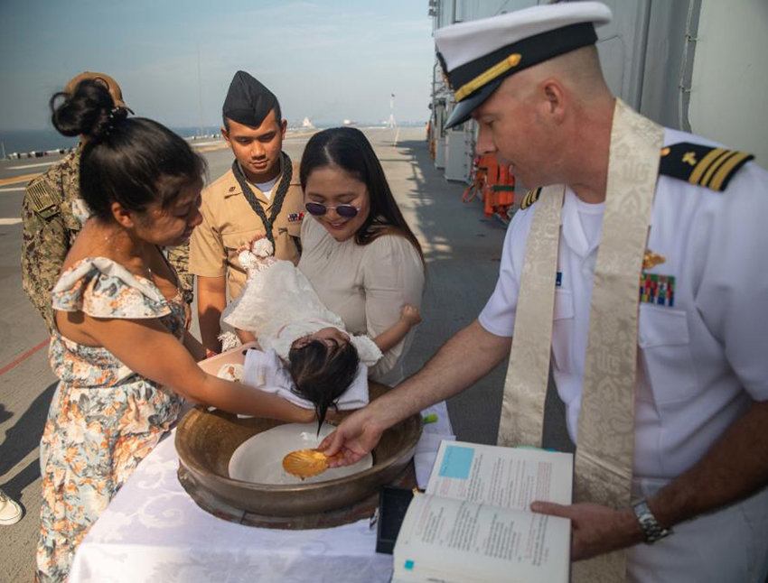 Sailors with the U.S. Navy and family attend a baptism in a bell at sea