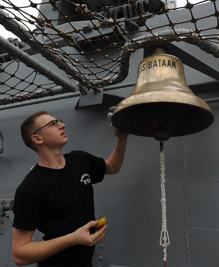 A sailor with the U.S. Navy polishes a ship's bell with lemon